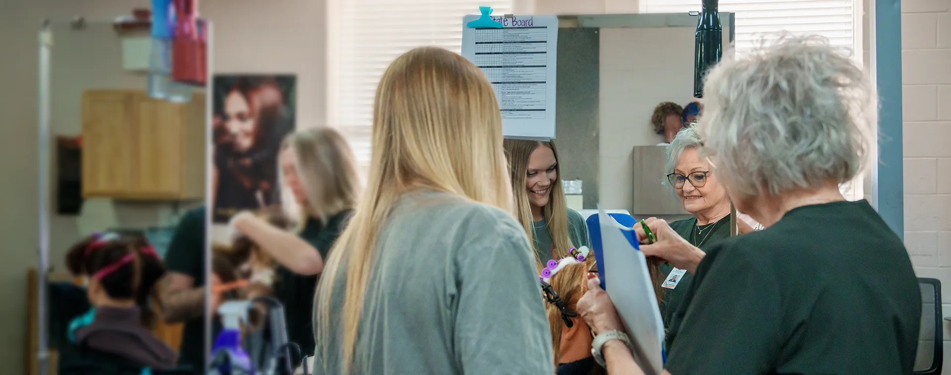 Instructor reviews hairstyling work with students in a cosmetology classroom salon near mirrored stations.