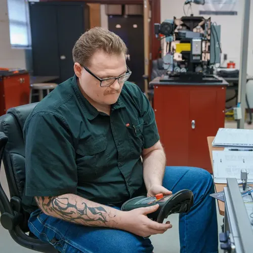 Student operates a handheld controller while seated beside an automated manufacturing training system.