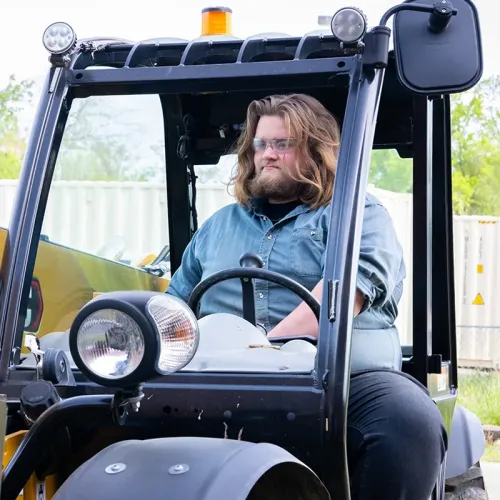 Student wearing safety glasses operates a forklift outdoors.