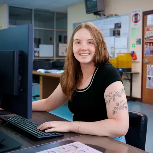 Student seated at a computer workstation in a graphic design classroom.